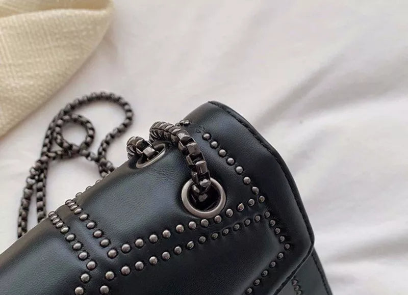 Schwarze Ledertasche mit Nieten und Kettenriemen auf weißem Hintergrund.