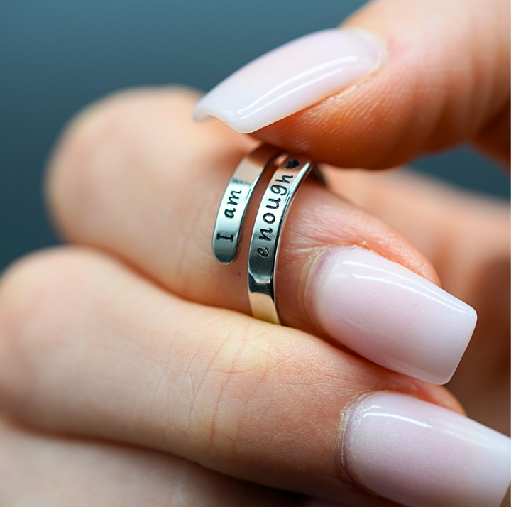 Silberner Motivationsring mit Gravur "I am enough", gehalten von Hand mit rosa Maniküre.