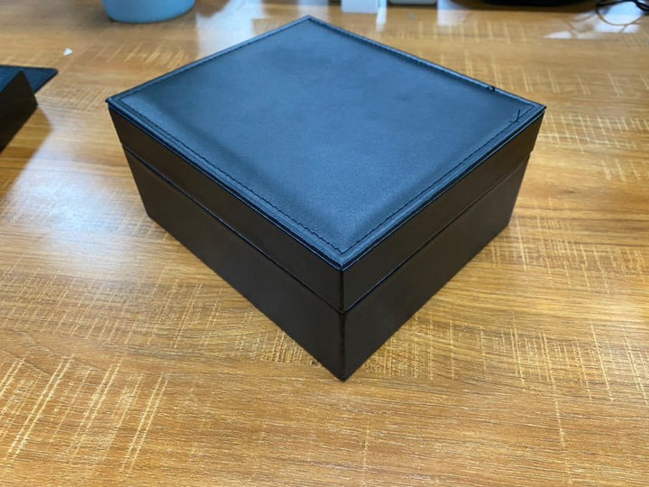 Schwarze Lederbox auf Holztisch, quadratisch, Aufbewahrung, elegant, hochwertig, Geschenkbox.