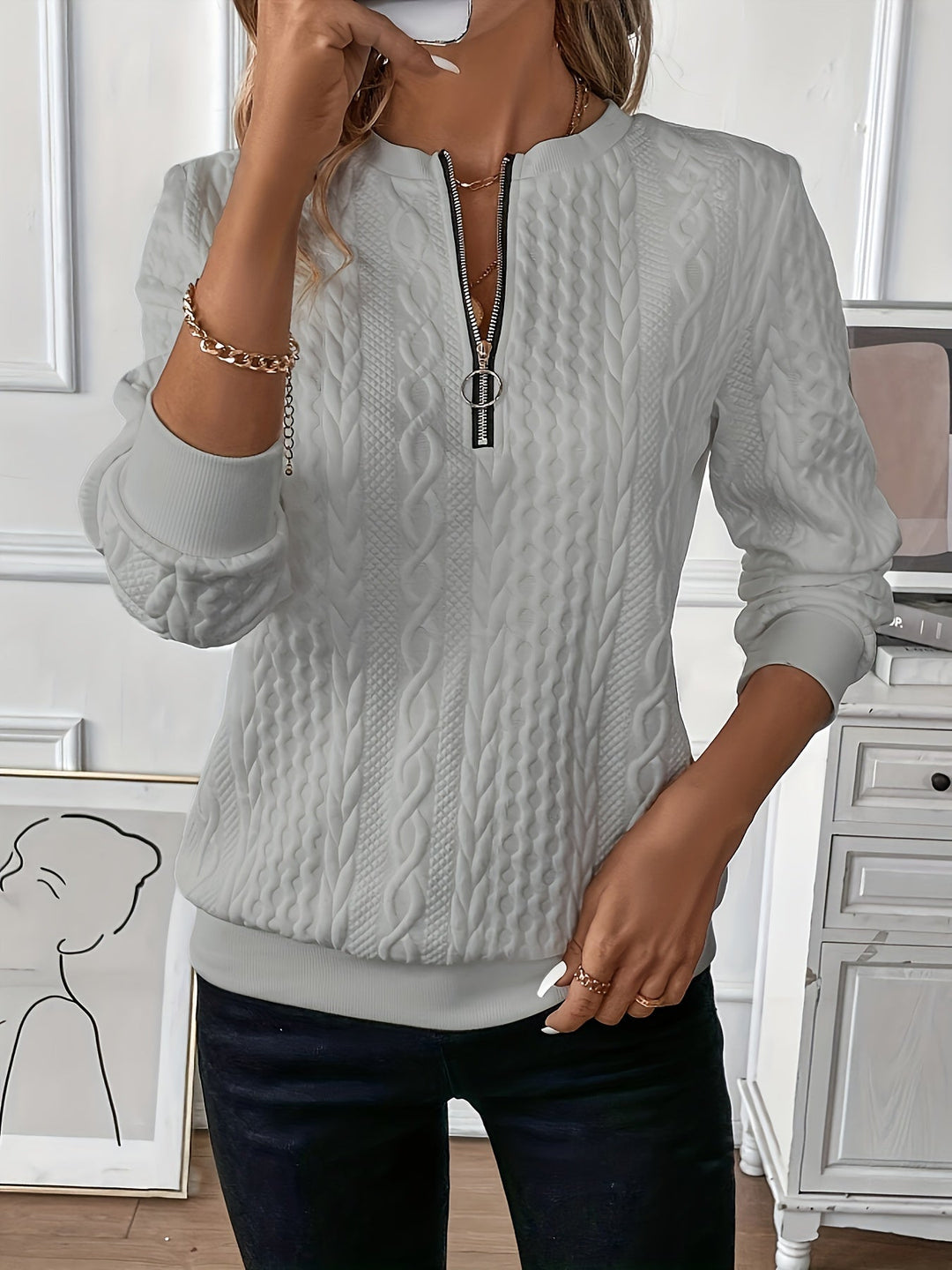 Frau trägt weißen Strickpullover mit Zopfmuster, Reißverschluss und Kette, modisch elegant.
