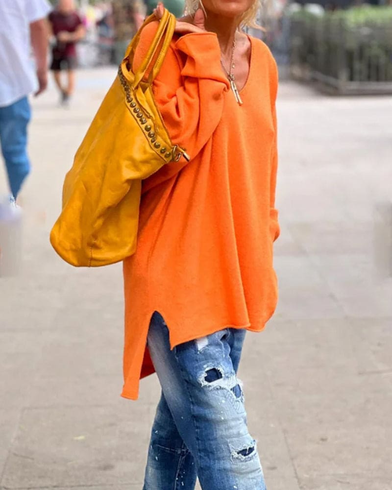 Frau in orangefarbenem Pullover, zerrissene Jeans, gelbe Tasche, lässige Straßenmode.