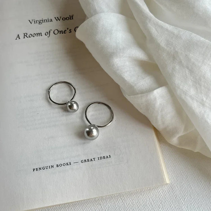 Silberne Ohrringe auf Buchseite, Virginia Woolf, A Room of One's Own, eleganter Schmuck, minimalistisch.
