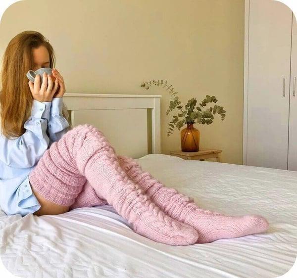 Frau in rosa gestrickten Wollsocken auf Bett, gemütlich, Wintermode, Innenraum.