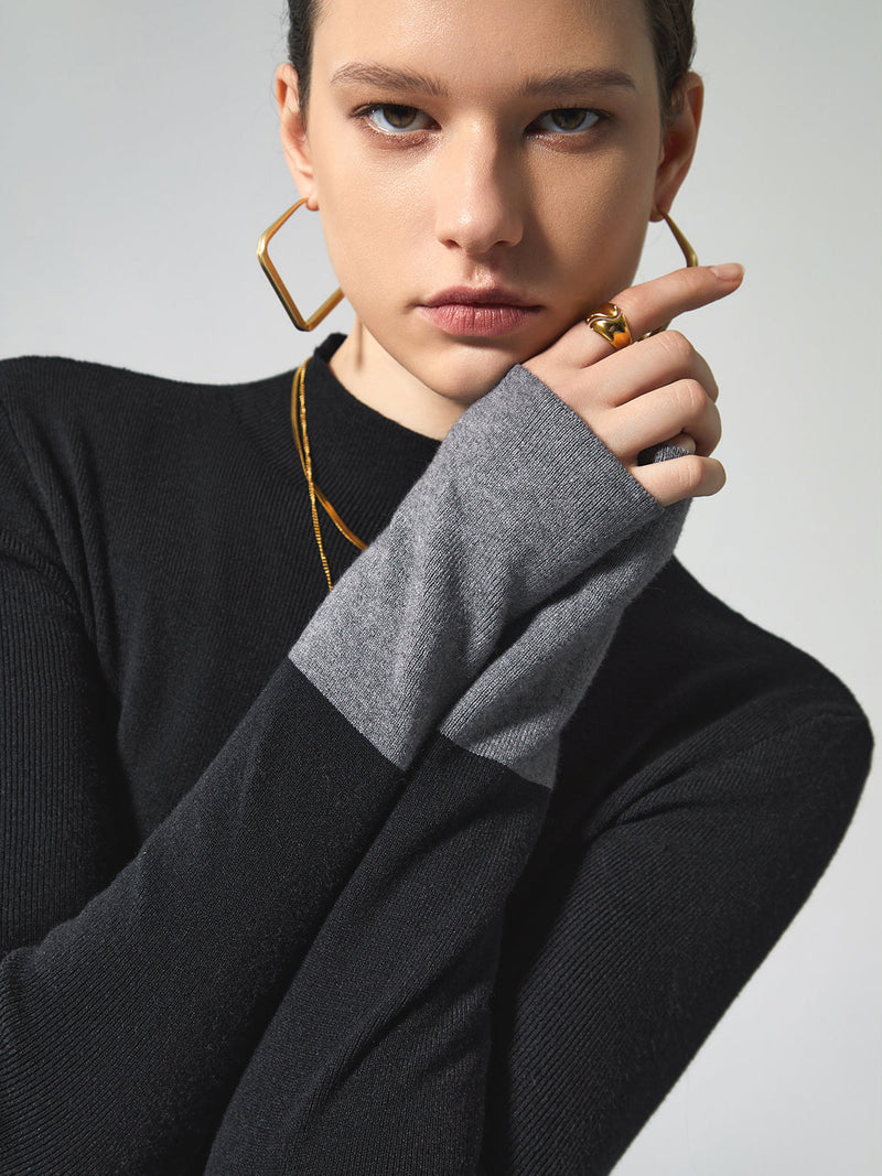 Frau in schwarzem Pullover mit grauen Ärmeln, goldene Ohrringe, modisches Accessoire.