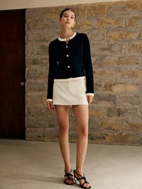 Frau in schwarzer Strickjacke und weißem Rock, elegante Mode, Innenaufnahme.