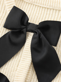 Schwarze Schleife auf cremefarbenem Strickpullover, elegantes Accessoire, modisches Detail.