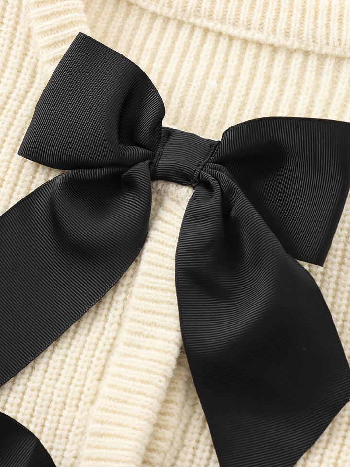 Schwarze Schleife auf cremefarbenem Strickpullover, elegantes Accessoire, modisches Detail.