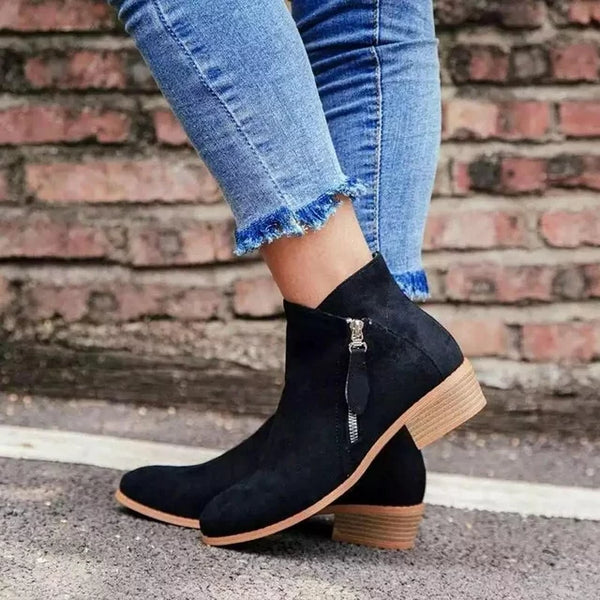 Schwarze Wildleder-Stiefeletten mit Reißverschluss, Damenmode, lässig, Jeans, Ziegelwand.