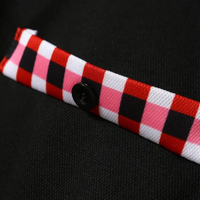 Schwarzer Stoff mit rot-weiß-schwarzem Karomuster und Knopf, Textildesign, Nahaufnahme.