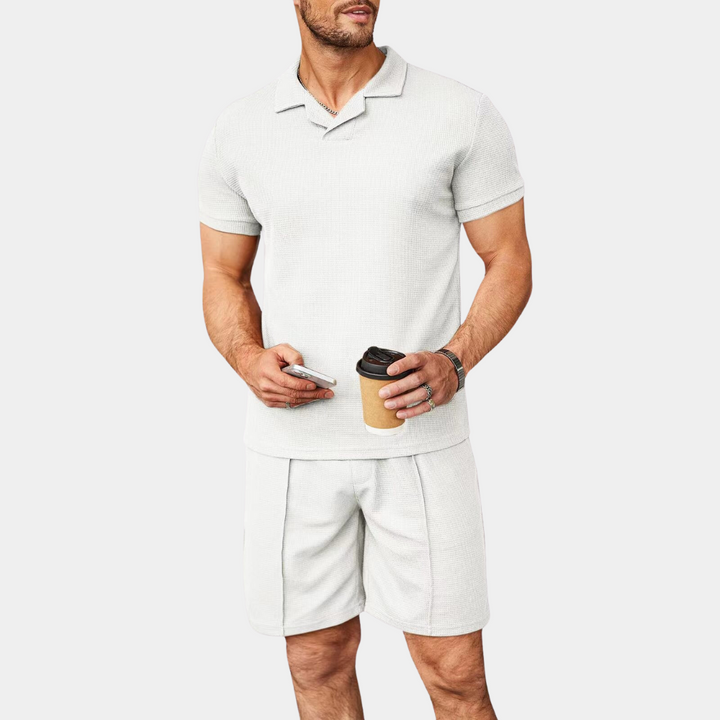 Mann in weißem Poloshirt und Shorts, hält Kaffeebecher, Sommermode, Freizeitkleidung.