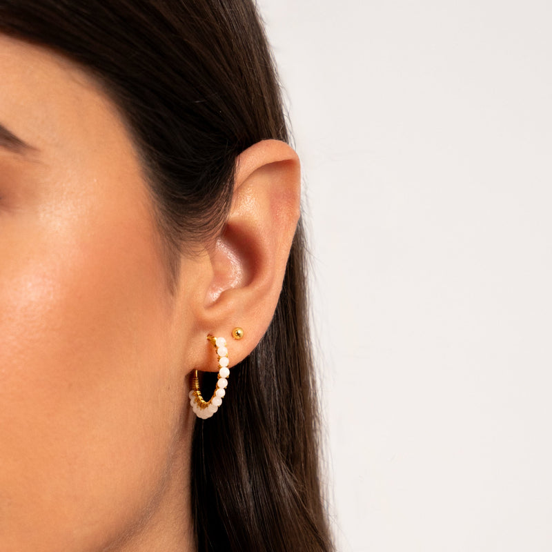Ohrring mit weißen Perlen und goldenen Details am Ohr einer Frau, Nahaufnahme.
