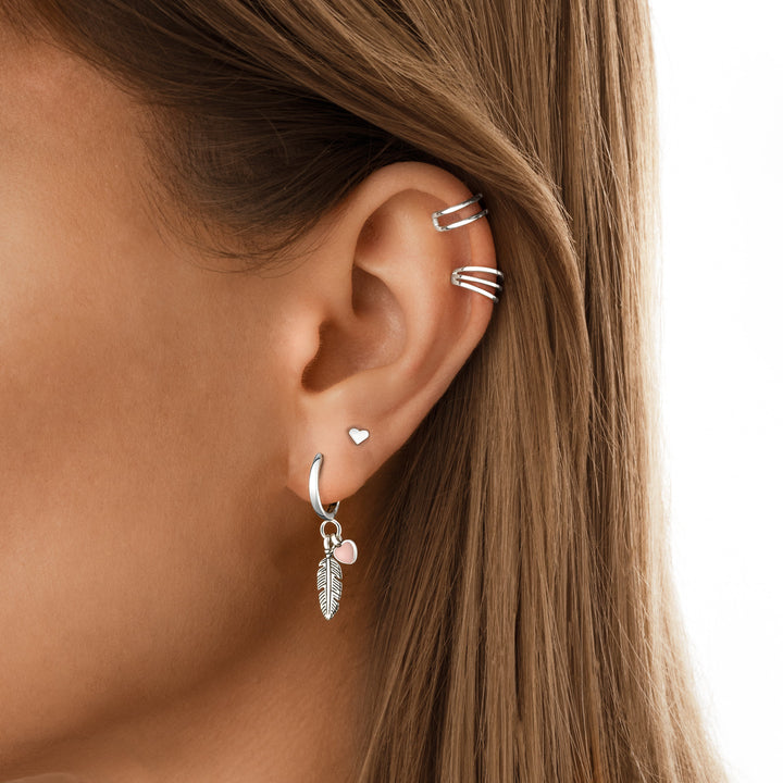 Frauenohr mit silbernen Ohrringen und Herzanhänger, modischer Schmuck, Nahaufnahme.