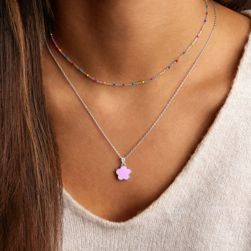 Frau mit zwei Halsketten, bunte Perlenkette und silberne Kette mit rosa Blumenanhänger.