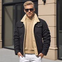 Mann in schwarzer Jacke mit beigem Futter, Sonnenbrille, vor modernem Gebäude.