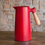 Rote Thermoskanne mit Holzgriff, skandinavisches Design, auf Holztisch vor Ziegelwand.