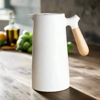 Weiße nordische Thermoskanne mit Holzgriff auf Holztisch, stilvolles Küchendesign.