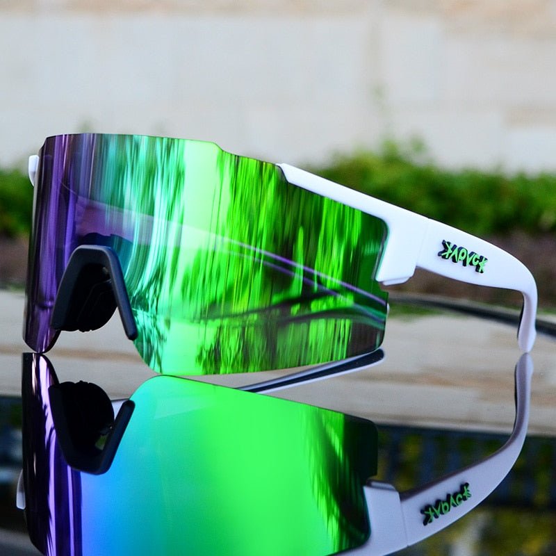Weiße Sportsonnenbrille mit grünen und violetten verspiegelten Gläsern auf reflektierender Oberfläche.