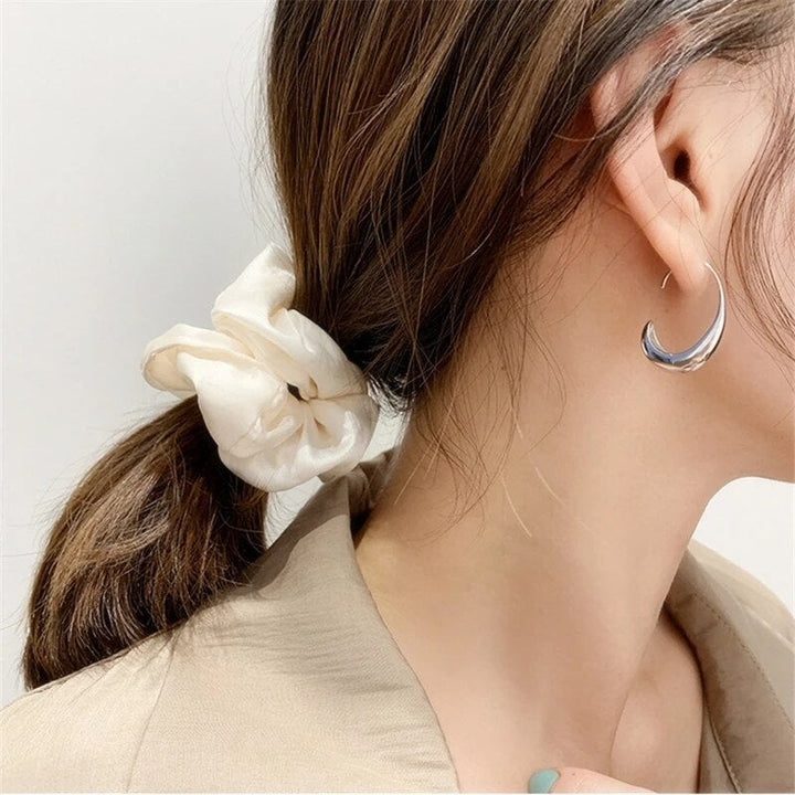 Frau mit beigem Haargummi und silbernem Ohrring, eleganter Look, Modeaccessoires.