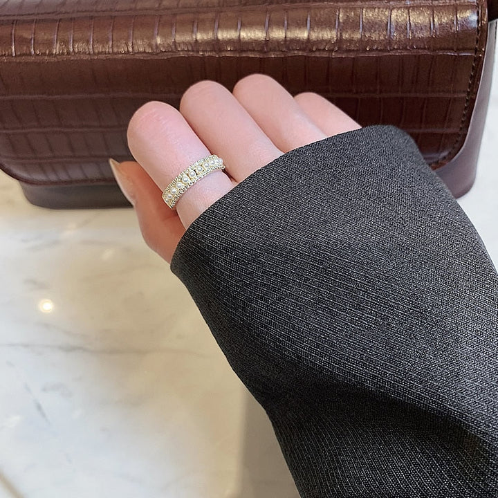 Hand mit funkelndem Diamantring vor brauner Lederhandtasche auf Marmortisch.