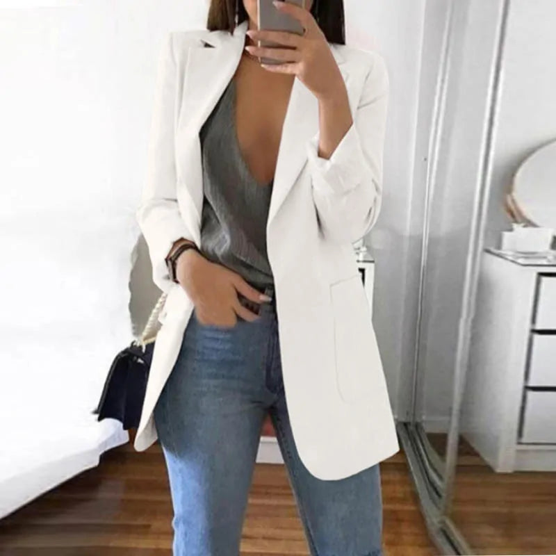 Frau in weißem Blazer, grauem Top und blauer Jeans, Spiegel-Selfie, modisch, elegant.