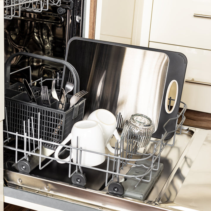 Offene Spülmaschine mit Geschirrkorb, Besteck, Tassen und Schneidebrett aus Edelstahl.