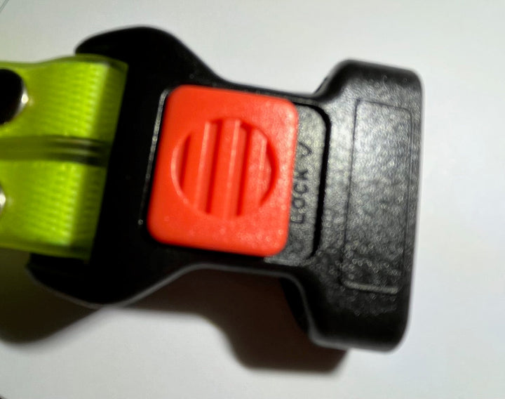 Schwarze Kunststoffschnalle mit rotem Verschluss auf gelbem Gurtband, Sicherheitsverschluss.