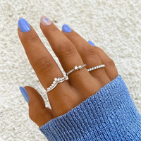 Frau mit blauen Nägeln trägt drei silberne Ringe, einer mit Stern, auf blauer Strickjacke.