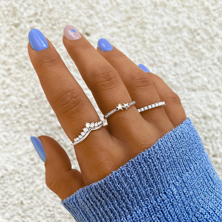 Frau mit blauen Nägeln trägt drei silberne Ringe, einer mit Stern, auf blauer Strickjacke.