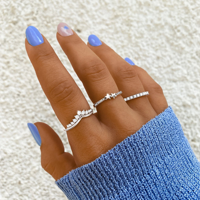 Frau mit blauen Nägeln trägt drei silberne Ringe, einer mit Stern, auf blauer Strickjacke.