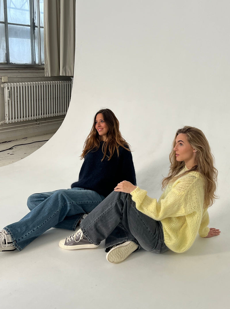 Zwei Frauen in lässigen Pullovern und Jeans posieren auf weißem Hintergrund im Fotostudio.