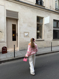 Frau in rosa-weißem Pullover und weißer Hose, trägt rosa Tasche, geht auf Pariser Straße.