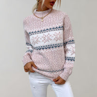 Frau in rosa Strickpullover mit Schneeflockenmuster, goldene Halskette, weiße Jeans.