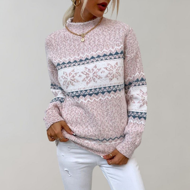 Frau in rosa Strickpullover mit Schneeflockenmuster, goldene Halskette, weiße Jeans.