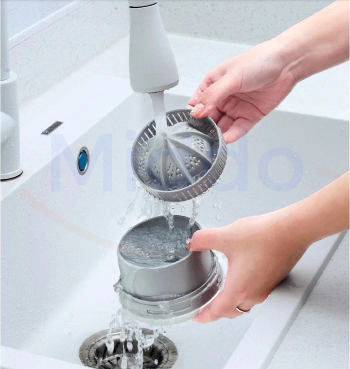 Person reinigt silberne Saftpresse unter Wasserhahn in weißem Waschbecken.