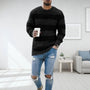 Mann in schwarzem Strickpullover, zerrissene Jeans, hält Kaffeetasse, modernes Wohnzimmer.