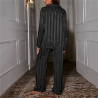 Frau in schwarzem gestreiftem Satin-Pyjama im Flur, elegante Nachtwäsche, gemütlich.