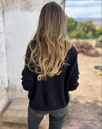 Frau in schwarzem V-Ausschnitt-Pullover, lange Ärmel, blonde Haare, draußen stehend.