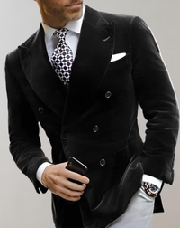 Mann im schwarzen Samt-Doppelreiher-Anzug mit gemusterter Krawatte und Smartphone in der Hand.