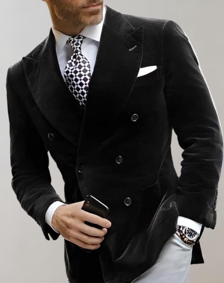 Mann im schwarzen Samt-Doppelreiher-Anzug mit gemusterter Krawatte und Smartphone in der Hand.