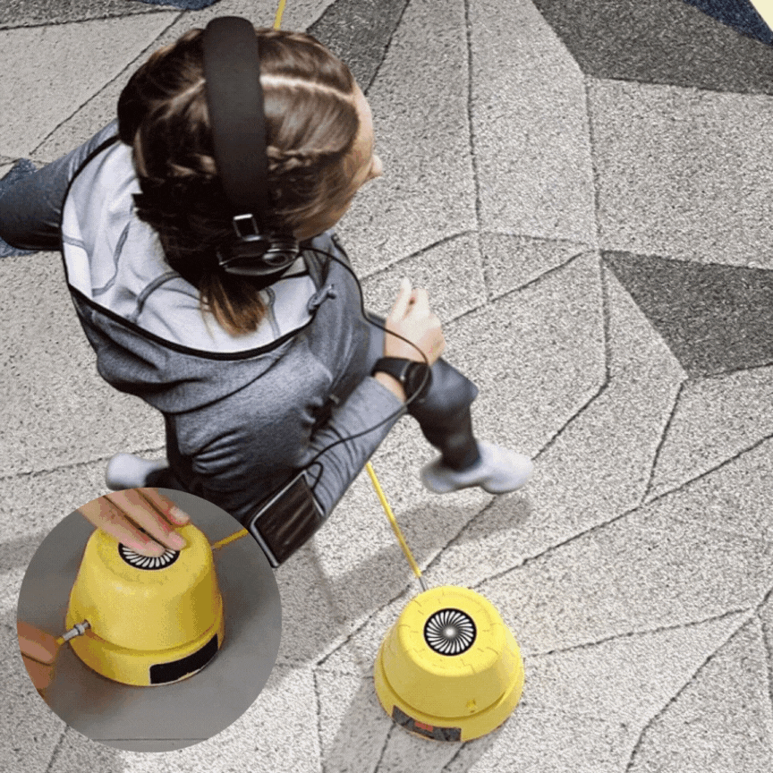 Person mit Kopfhörern nutzt gelben Bodenreinigungsroboter auf grauem Teppich.