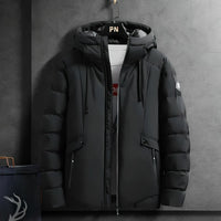 Schwarze Winterjacke mit Kapuze, Reißverschlüssen und Taschen, hängend an grauer Wand.