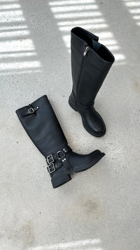 Schwarze Lederstiefel mit Schnallen, Reißverschluss, flachem Absatz auf Betonboden.