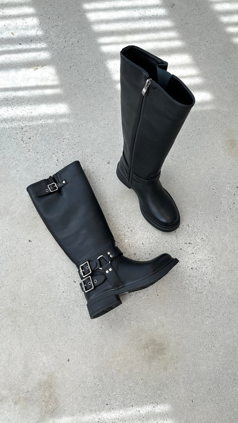 Schwarze Lederstiefel mit Schnallen, Reißverschluss, flachem Absatz auf Betonboden.