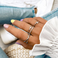 Frau mit silbernen Ringen, Kreuzdesign, pastellfarbene Nägel, weiße Bluse, Jeans.