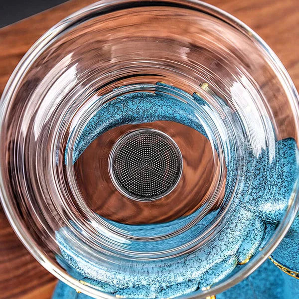 Glas-Teekanne mit Sieb, transparent, auf blauem Untersetzer, Holzuntergrund, modern, stilvoll.