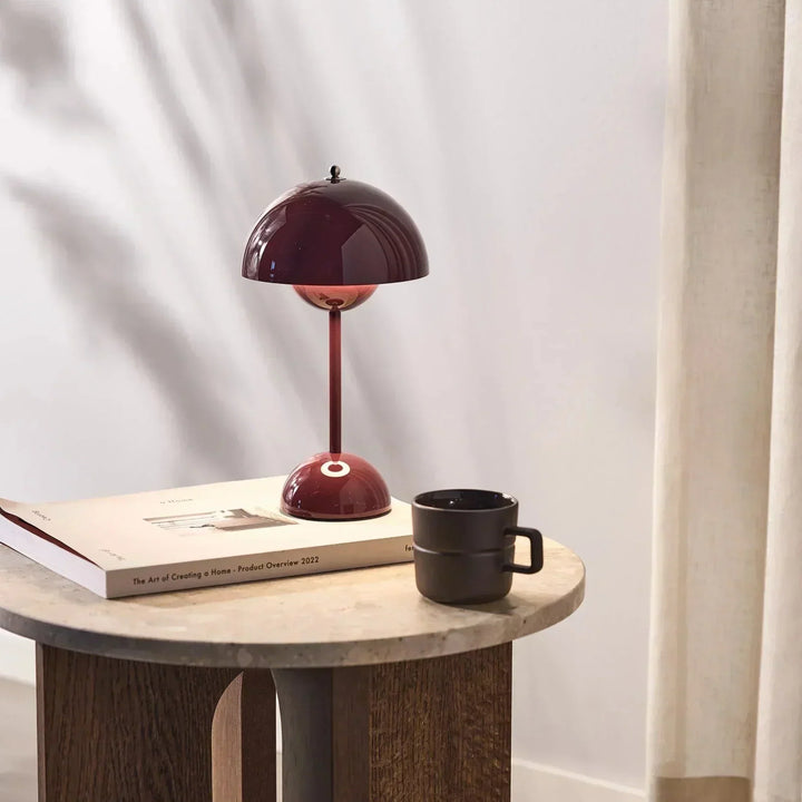 Rote Tischlampe aus Metall auf Holztisch mit Buch und schwarzer Tasse, modernes Innendesign.