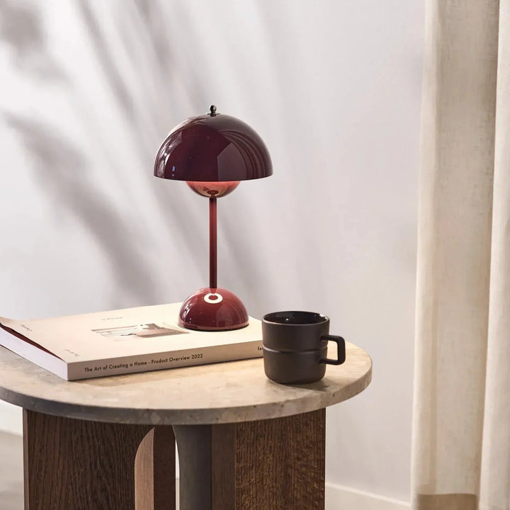 Rote Tischlampe aus Metall auf Holztisch mit Buch und schwarzer Tasse, modernes Innendesign.