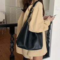 Frau mit schwarzer Ledertasche, beige Jacke, Smartphone, modernes Interieur.
