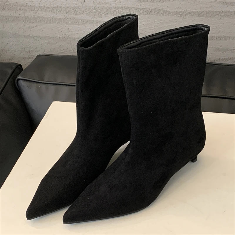 Schwarze Wildleder-Stiefeletten mit spitzem Absatz auf weißem Tisch, modisch und elegant.