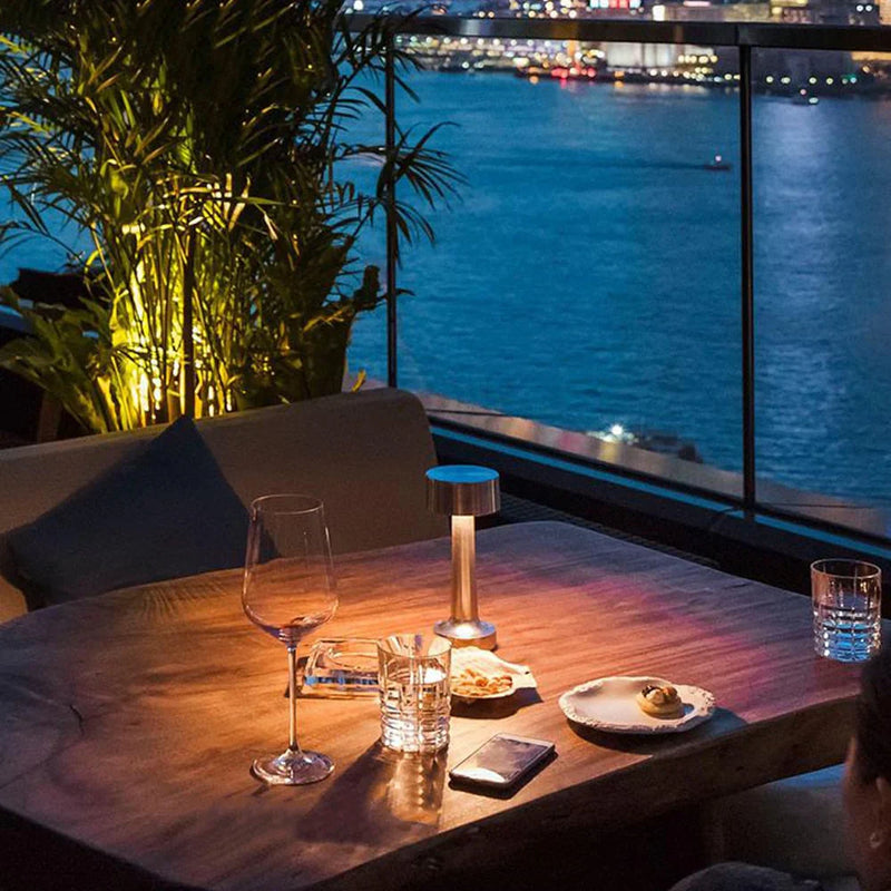 Terrasse bei Nacht mit Holztisch, Weinglas, Kerzenlicht, Blick auf beleuchtete Stadt und Fluss.